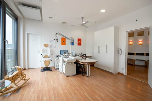Behandlungsraum mit Untersuchungsstuhl, bunten Bildern an der Wand und einem Holz-Schaukelmotorrad für Kinder