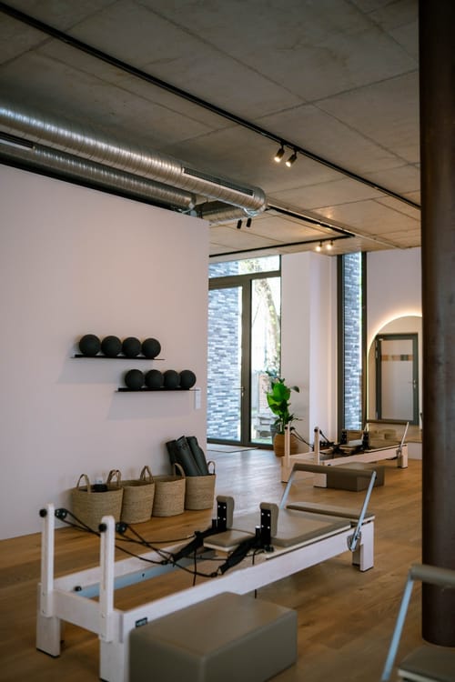 Trainingsraum mit Reformern, Bällen auf Wandregalen, Körben und Yogamatten unter einer Betondecke