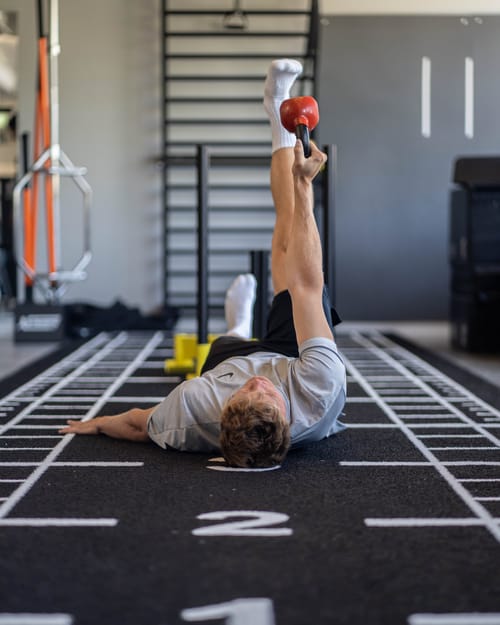 Sportler liegt bei einer Übung mit Kettlebell auf dem markierten Hallenboden