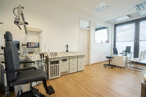 HNO-Behandlungsraum mit Untersuchungsstuhl, Mikroskop, Behandlungseinheit und Schreibtisch am Fenster