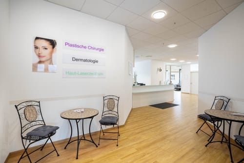 Eingangsbereich mit Bistrotischen und Wandschildern „Plastische Chirurgie“, „Dermatologie“ und „Haut-Laserzentrum“