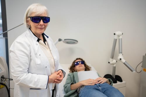 Ärztin im weißen Kittel mit Laserschutzbrille neben einer Patientin auf der Behandlungsliege