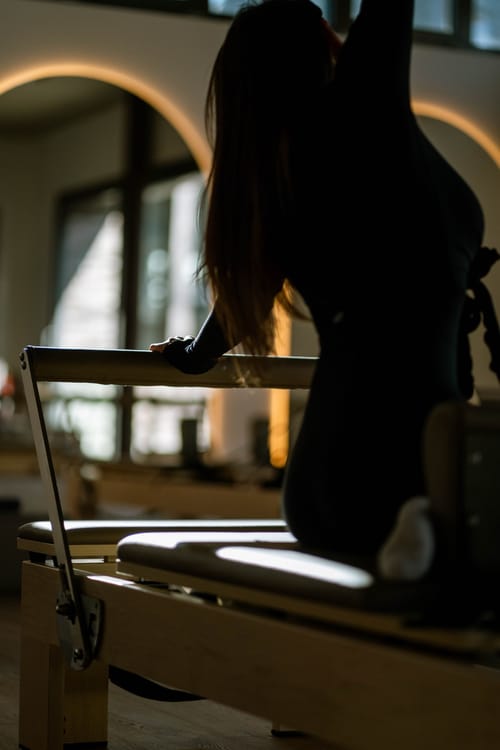 Silhouette einer Frau auf dem Reformer im Gegenlicht vor beleuchteten Bogenspiegeln