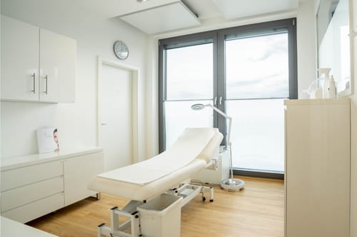 Weißer Behandlungsraum mit Liege, Lupenleuchte und Fenster